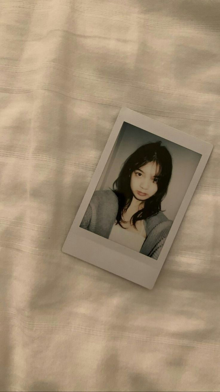 a polaroid photo of a young woman laying on a white sheet with her head turned to the side