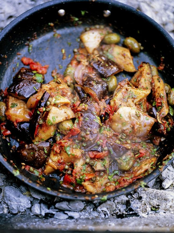 a skillet filled with food sitting on top of a stone slab covered in dirt