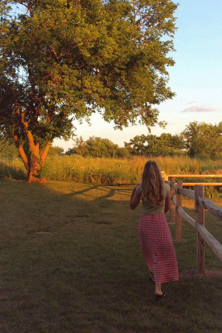 a girl in a red and white checkered dress leaning on a fence looking at the grass