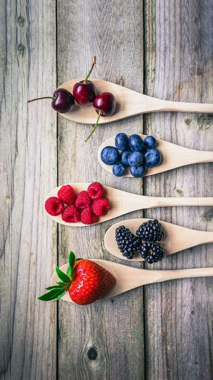 spoons filled with berries, raspberries and blueberries on top of a wooden table