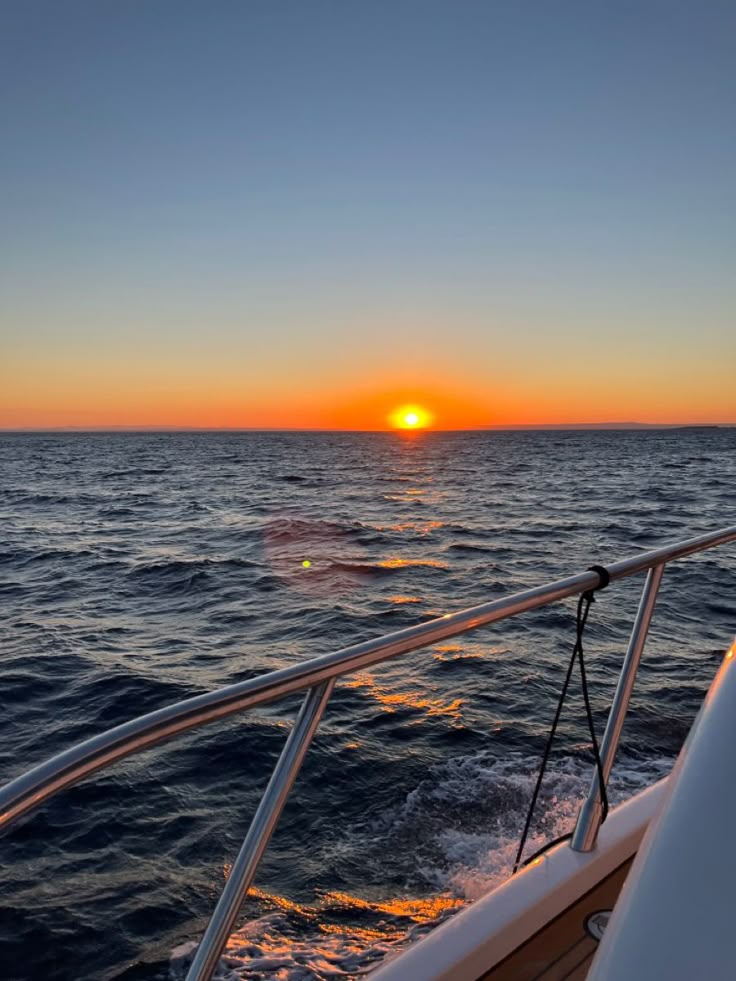 the sun is setting over the ocean on a boat