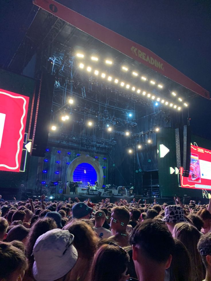 a large group of people at an outdoor concert with lights on and big screen in the background