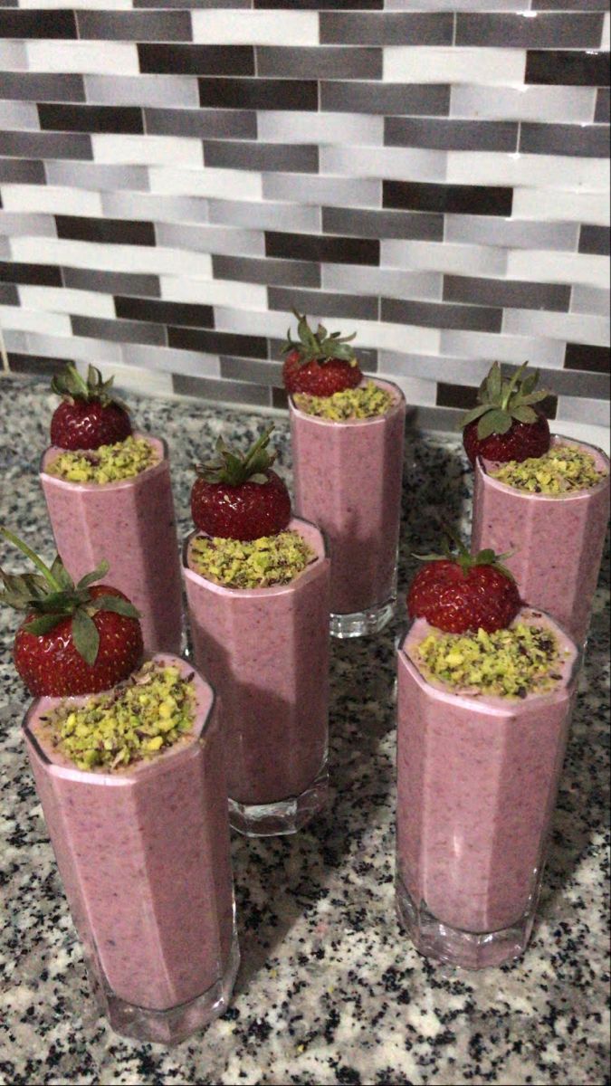 four glasses filled with smoothie and strawberries on top of a counter next to a tiled wall