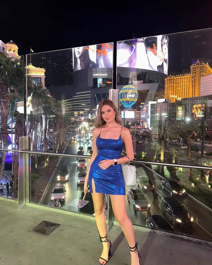 a woman in a blue dress standing on a balcony with cars and buildings behind her