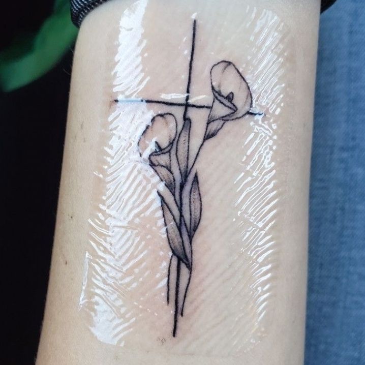 a cross with two flowers on the side of the arm and behind it is a tattoo