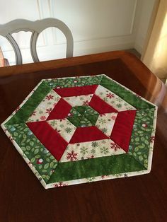 a green and red quilted table topper on a wooden table with a white chair in the background