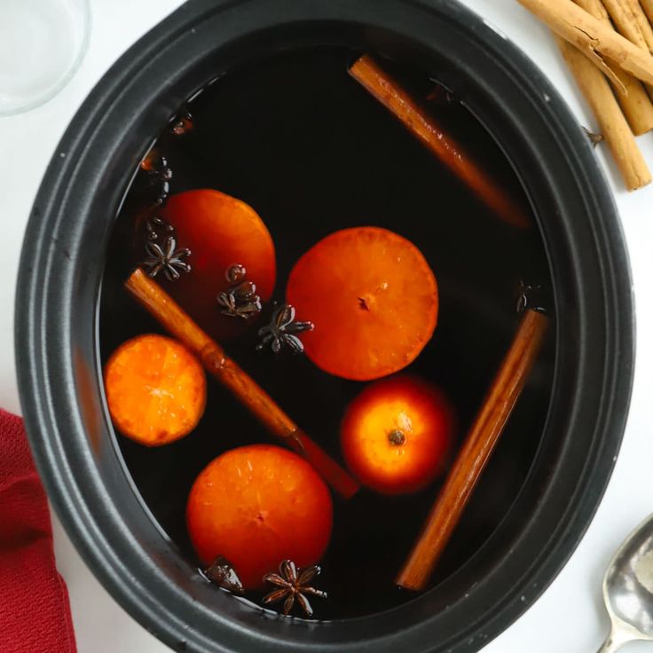 some cinnamon sticks and oranges are in a black pot with water on the table