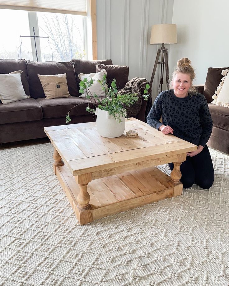 a woman sitting on the floor in front of a coffee table with a potted plant