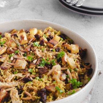 a white bowl filled with rice and meat on top of a table next to silverware