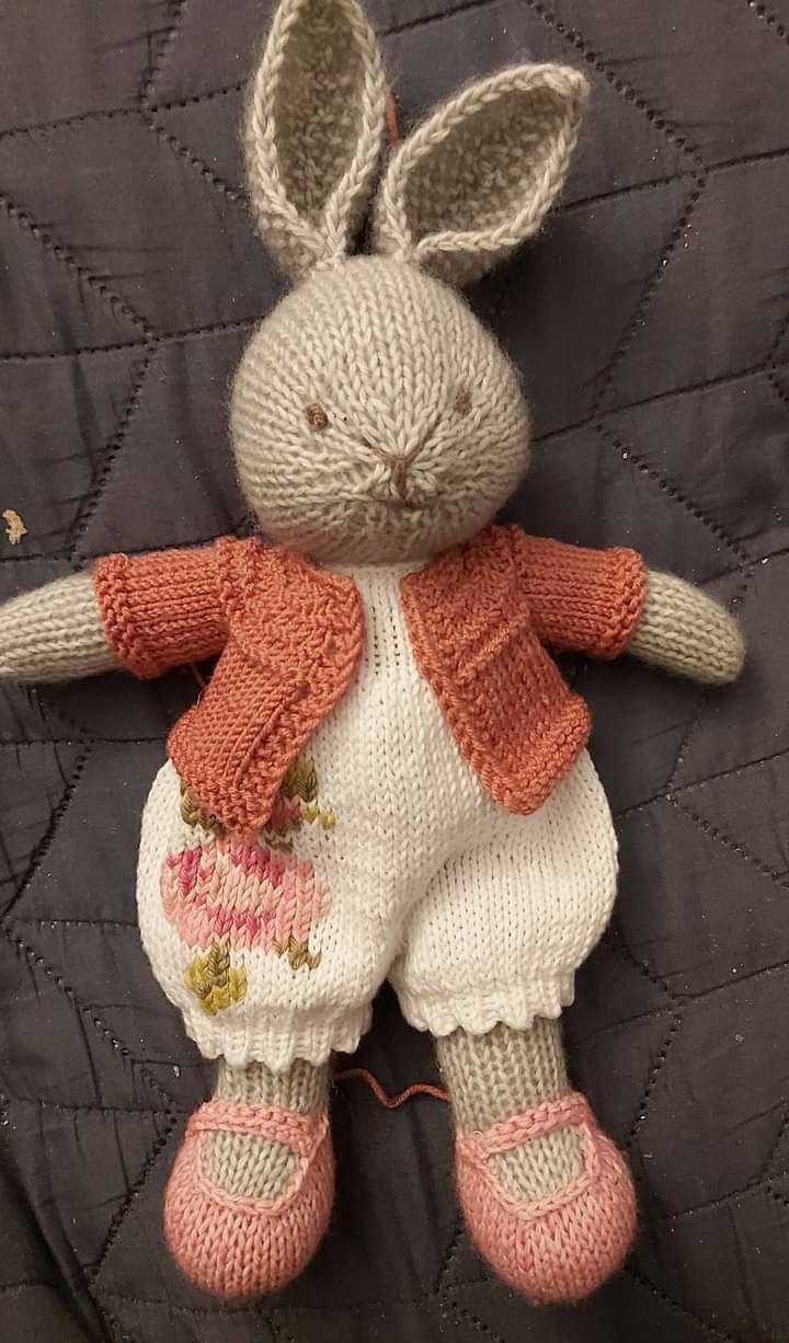 a knitted bunny doll laying on top of a quilt