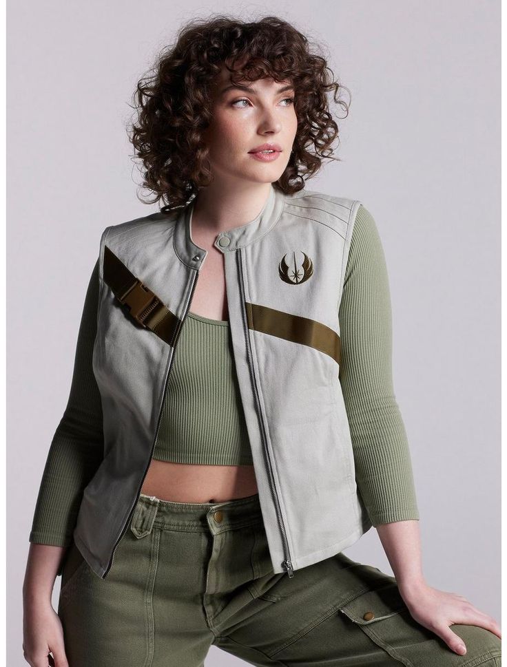 a woman with curly hair wearing green pants and a star wars jacket is posing for the camera