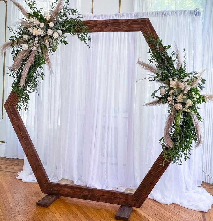 a wooden frame with flowers and greenery on the floor in front of a white curtain