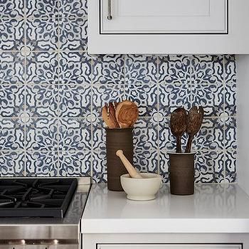 a stove top oven sitting next to a wall covered in white tiles and wooden utensils