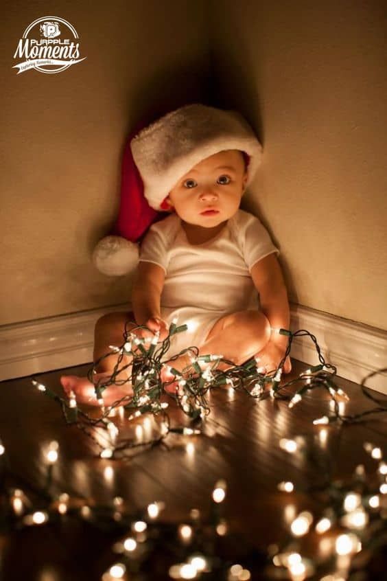 a baby is sitting on the floor surrounded by christmas lights with a santa hat on