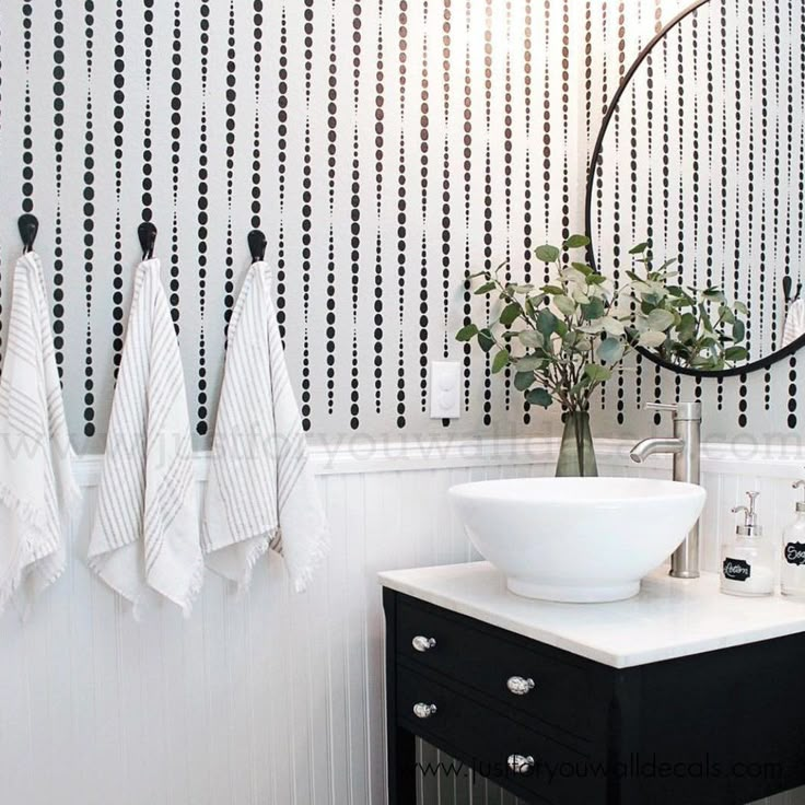 a bathroom with black and white wallpaper, two towels hanging on the hooks, a sink and a round mirror