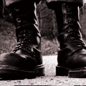 black and white photograph of man's legs in boots on the ground with grass behind them