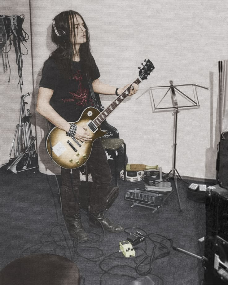 a man with dreadlocks playing an electric guitar in a recording studio, while another musician stands behind him