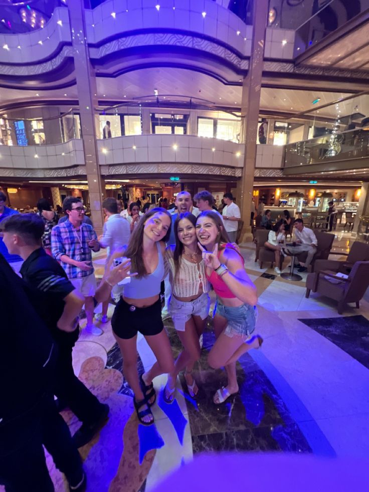 three girls are posing for the camera in front of a group of people at a party