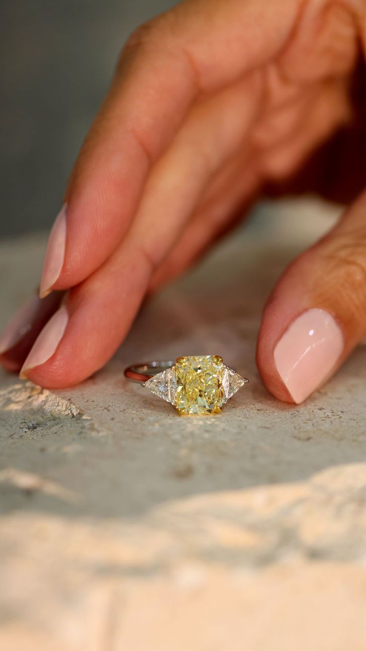 a woman's hand touching a yellow diamond on top of a white marble table