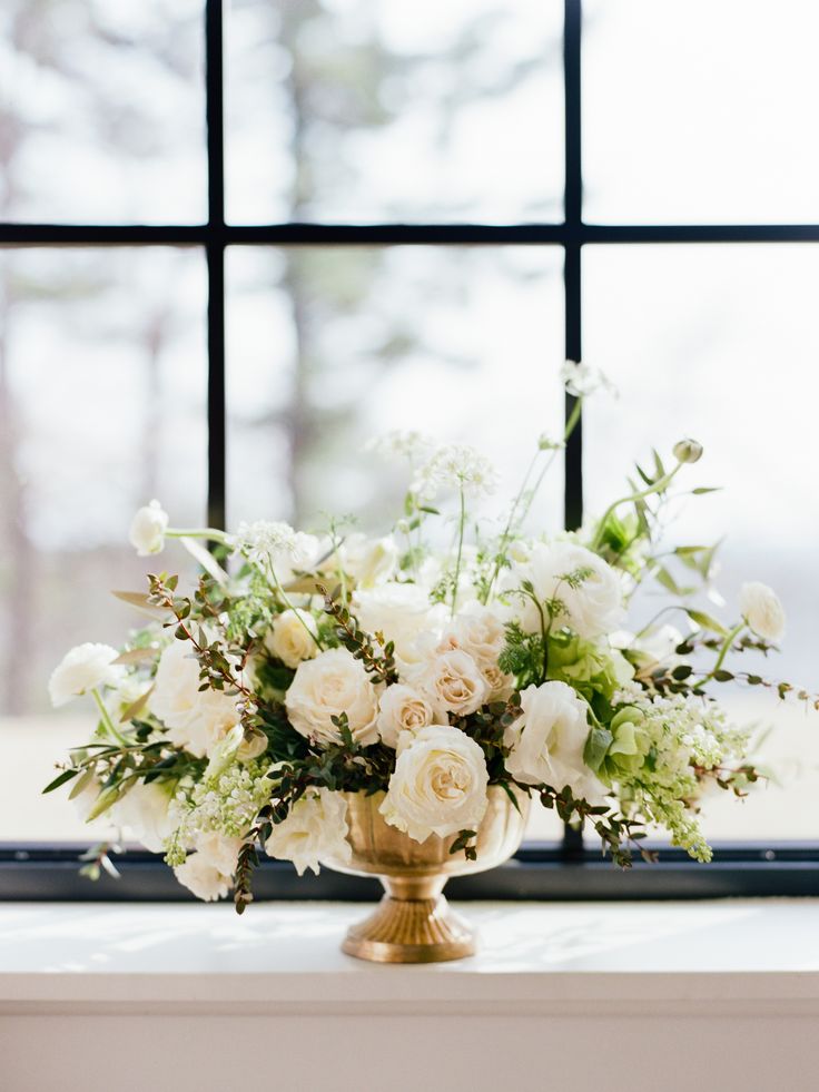 a vase filled with white flowers sitting on top of a table next to a window