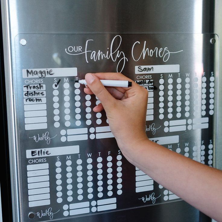 a person writing on a family chore chart with a white chalkboard in front of them