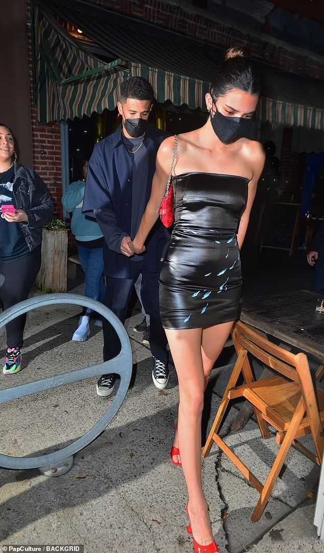 a woman wearing a black leather dress and mask walks down the street with two people behind her