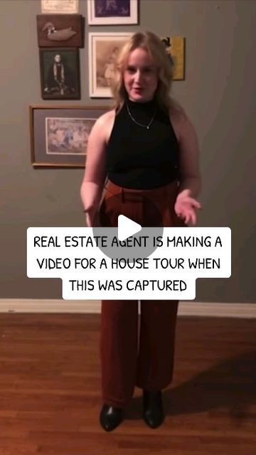 a woman is standing in front of a wall with pictures on it and the caption reads real estate agent is making a video for a house tour when this was captured