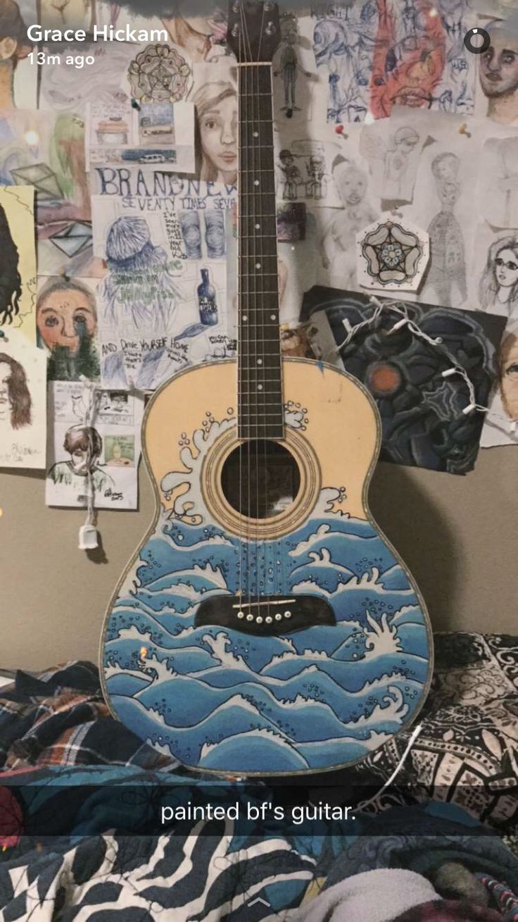 an acoustic guitar sitting on top of a bed covered in pictures and papers with the words painted by's guitar