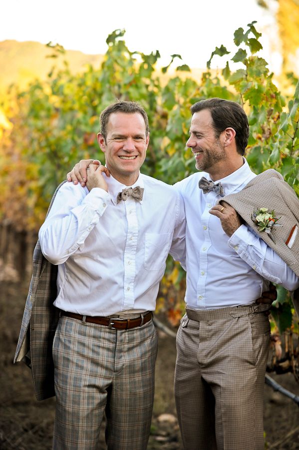 two men standing next to each other in the middle of a vineyard with vines behind them