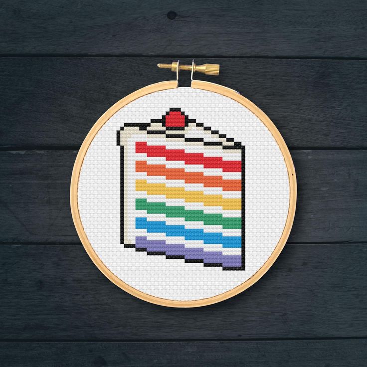 a cross stitch rainbow flag on a wooden wall hanging in front of a black background