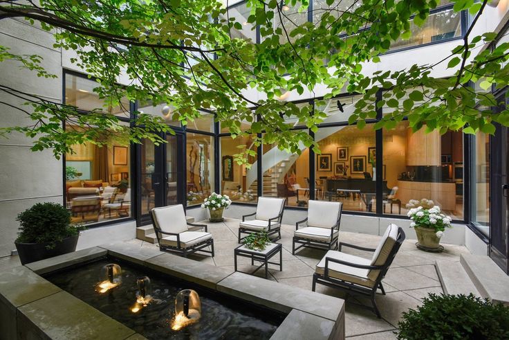 an outdoor living area with chairs, tables and water feature in the center surrounded by greenery