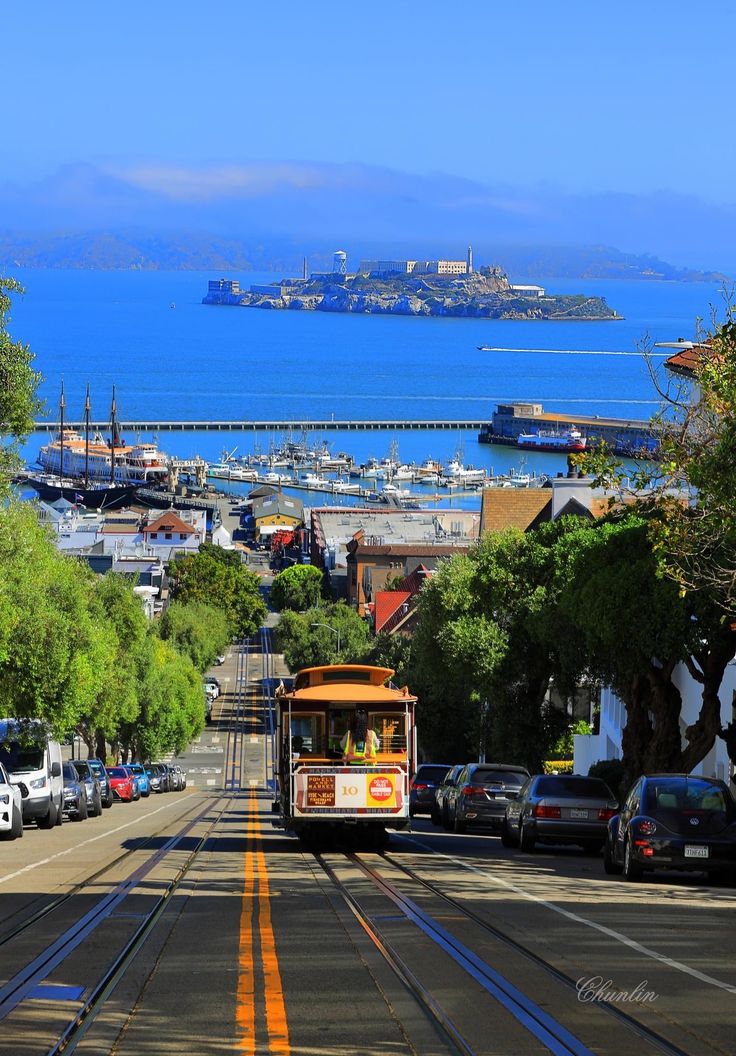 a trolley car traveling down the road near some cars and buildings with water in the background