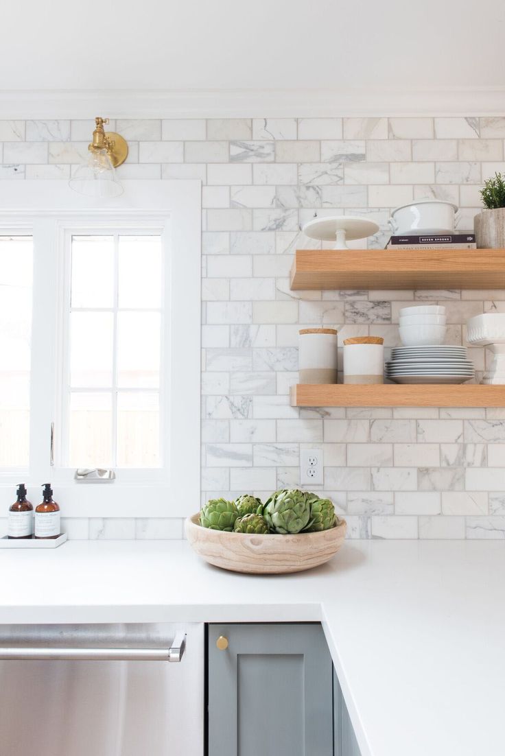 a white kitchen with open shelving above the sink and dishes on the counter top