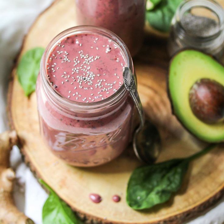 two mason jars filled with smoothie on top of a wooden cutting board next to an avocado