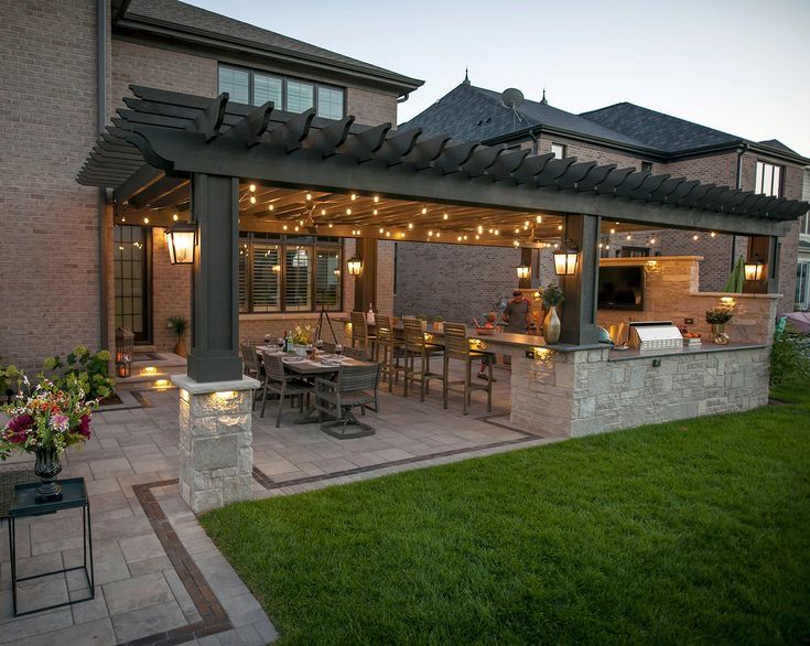 an outdoor kitchen and dining area is lit up at night with string lights on the roof