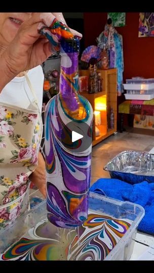 a woman is painting a glass bottle with colorful swirls on the outside and inside