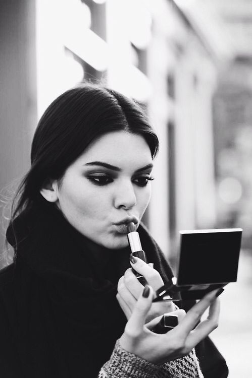 a woman is holding a lipstick and looking at her phone