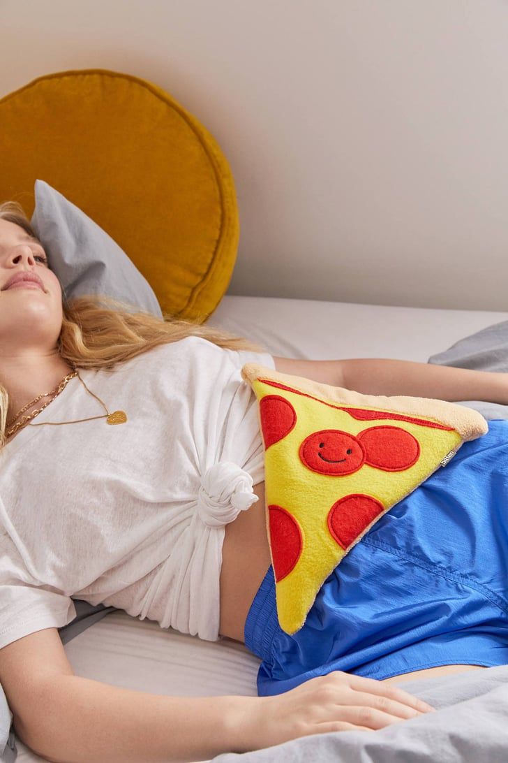 a woman laying on top of a bed next to a pillow with a slice of pizza on it