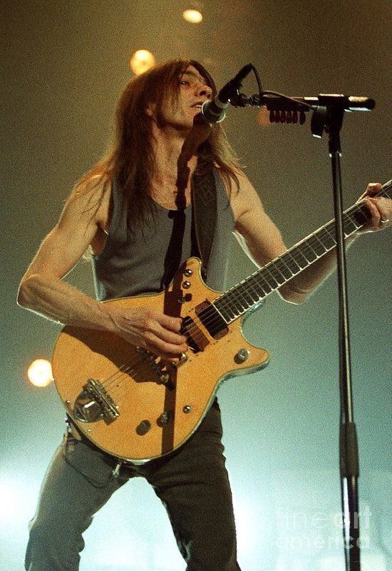 a man with long hair playing an electric guitar in front of a microphone on stage