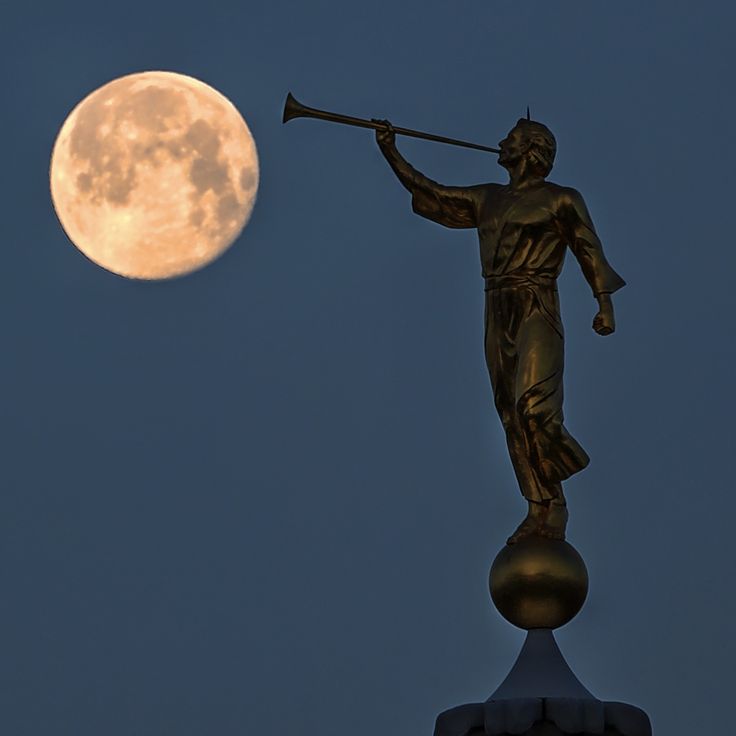 a statue is holding an instrument in front of the moon