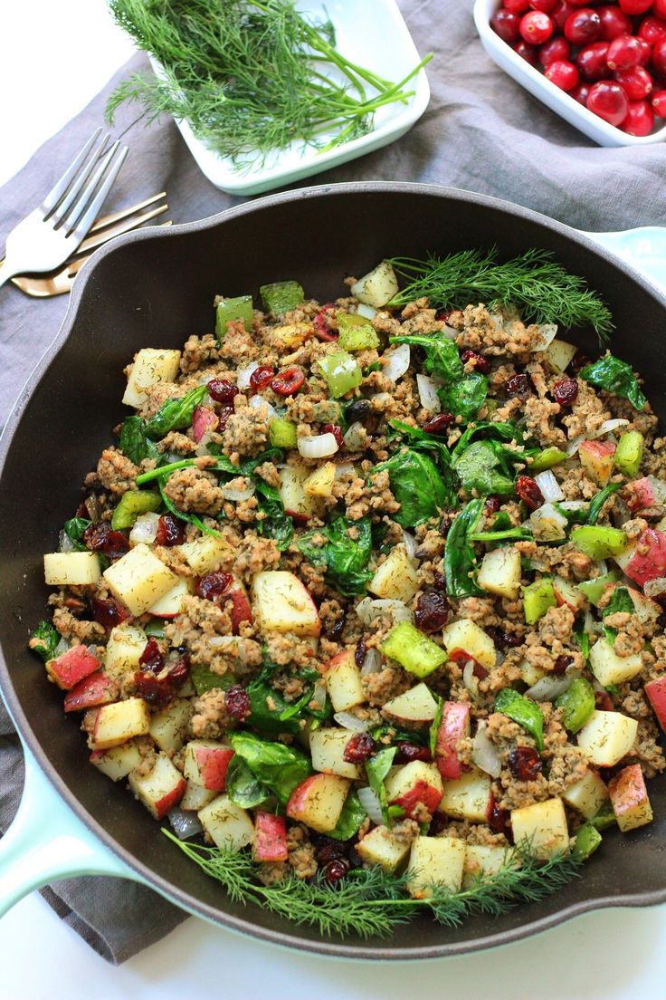 a skillet filled with meat, vegetables and cranberries on top of a table