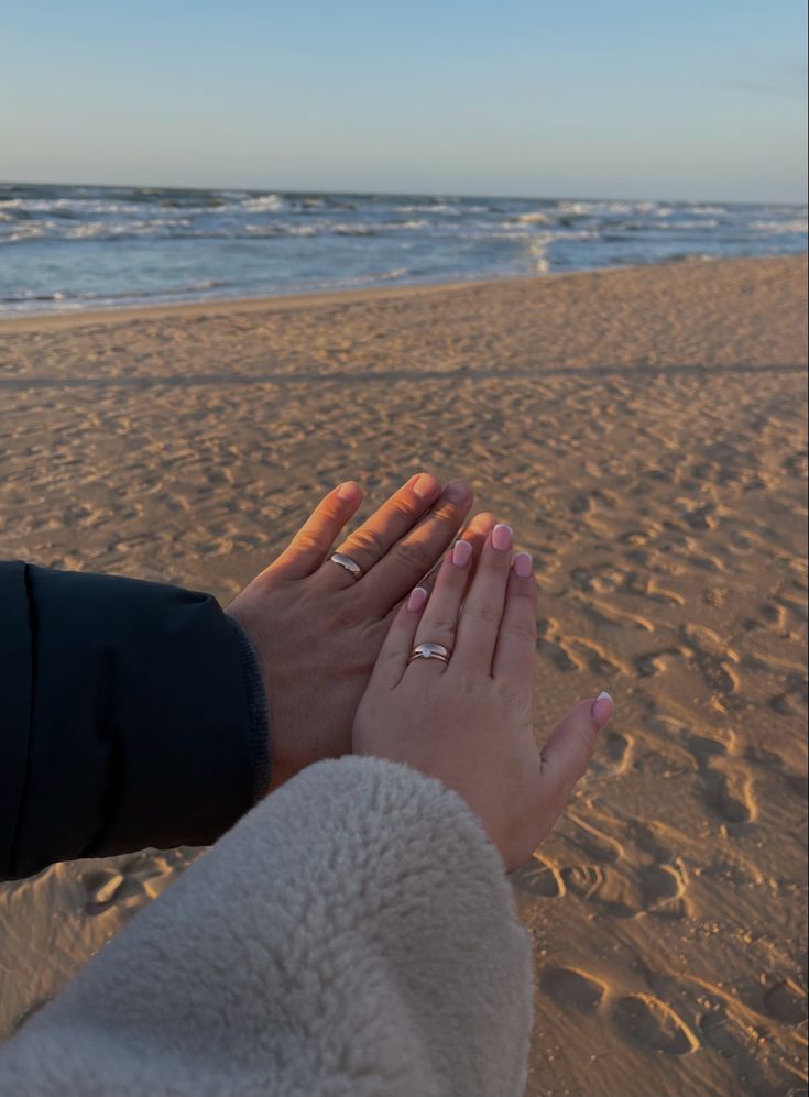 two people are holding hands on the beach