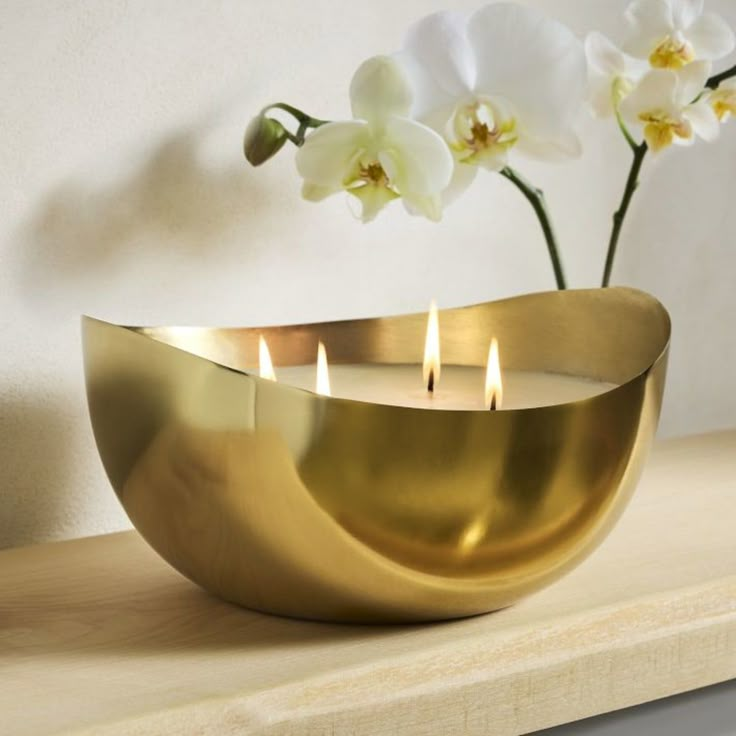 two candles are in a gold bowl on a shelf