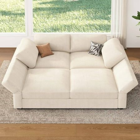 a white couch sitting on top of a wooden floor next to a window with grass outside