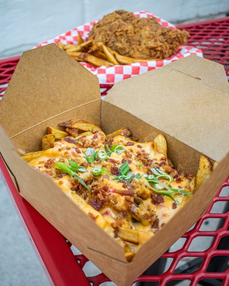 an open box of pizza sitting on top of a red table next to some fries