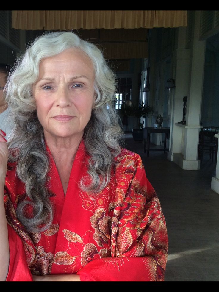 an older woman with grey hair and red dress holding a cell phone to her ear