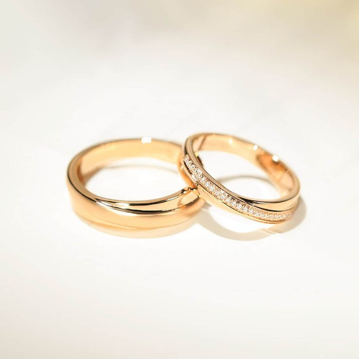 two gold wedding rings with diamonds on them sitting side by side against a white background