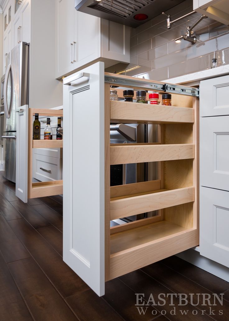 an open cabinet in the middle of a kitchen with white cabinets and wood flooring