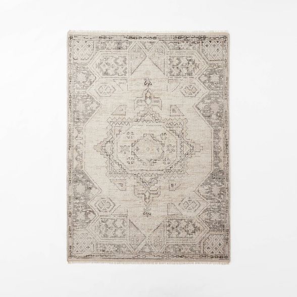 a beige rug with an intricate design on the bottom and sides, against a white wall