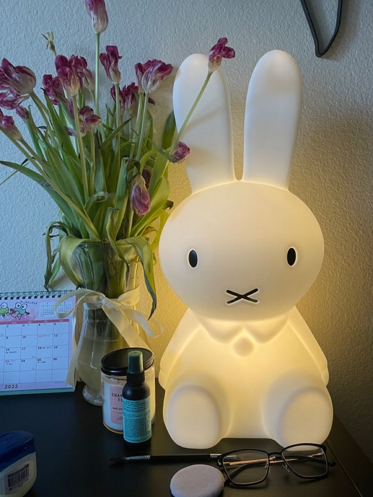 a white bunny lamp sitting on top of a desk next to a vase with flowers